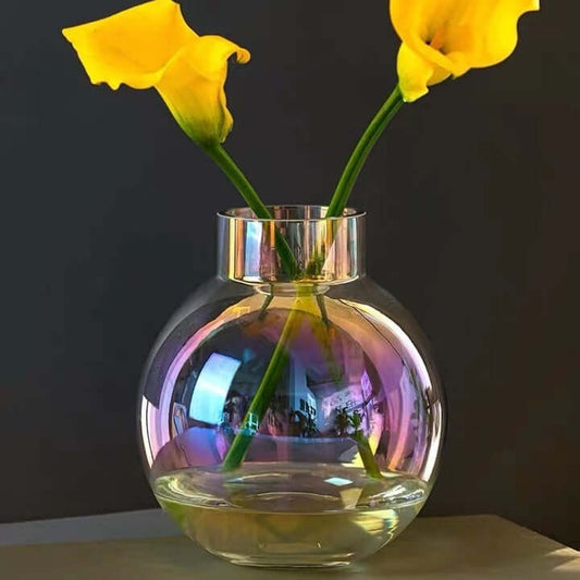 Iridescent glass vase with yellow flowers, showcasing color-shifting effects in soft lighting.